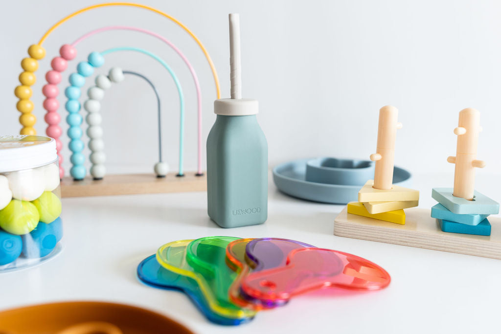 Colorful children's toys including a bottle, rainbow arch, and plastic shapes on a white surface.