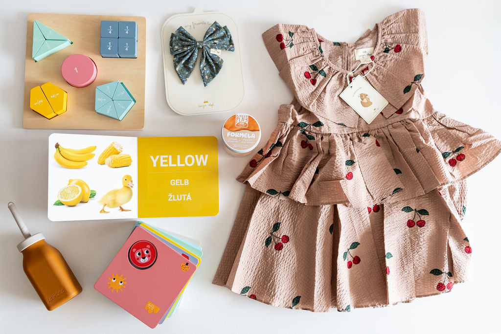 Children's dress with floral details on a white surface with educational toys and cards.